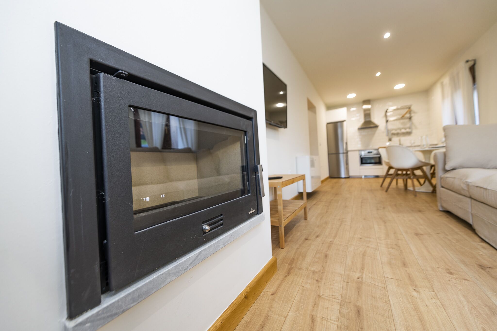 Una sala moderna con chimenea empotrada, piso de madera, un sofá y un comedor al fondo.