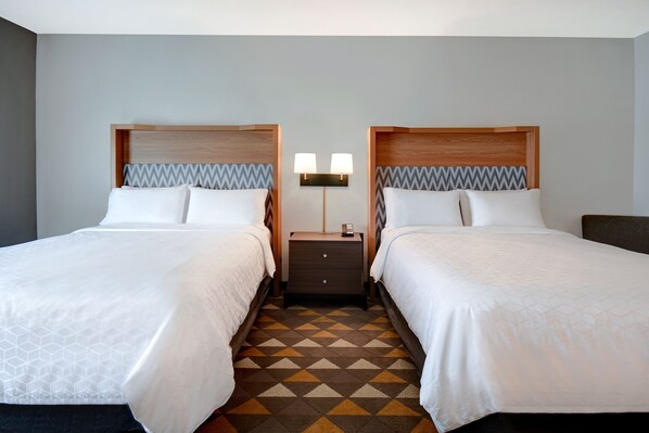 Una habitación de hotel con dos camas, una mesita de noche con lámparas y un suelo con estampado geométrico.