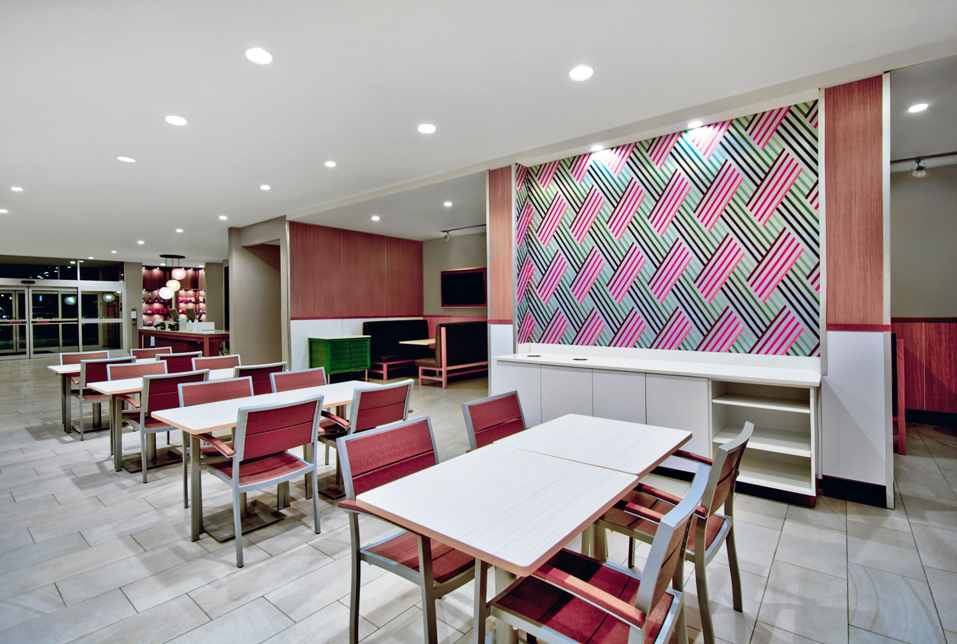 A modern dining area with tables and chairs, a kitchen area with a colorful geometric backsplash, and a seating area with a TV.