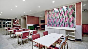 A modern dining area with tables and chairs, a kitchen area with a colorful geometric backsplash, and a seating area with a TV.