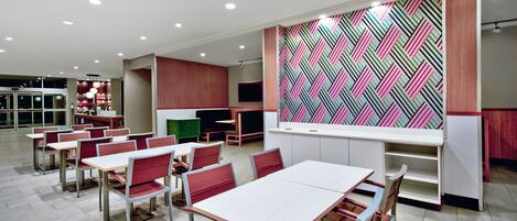 A modern dining area with tables and chairs, a kitchen area with a colorful geometric backsplash, and a seating area with a TV.