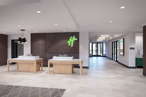 A hotel lobby with two reception desks, a green 'H' logo on the wall, and a corridor leading to guest rooms. - Holiday Inn Erie by IHG (Erie)