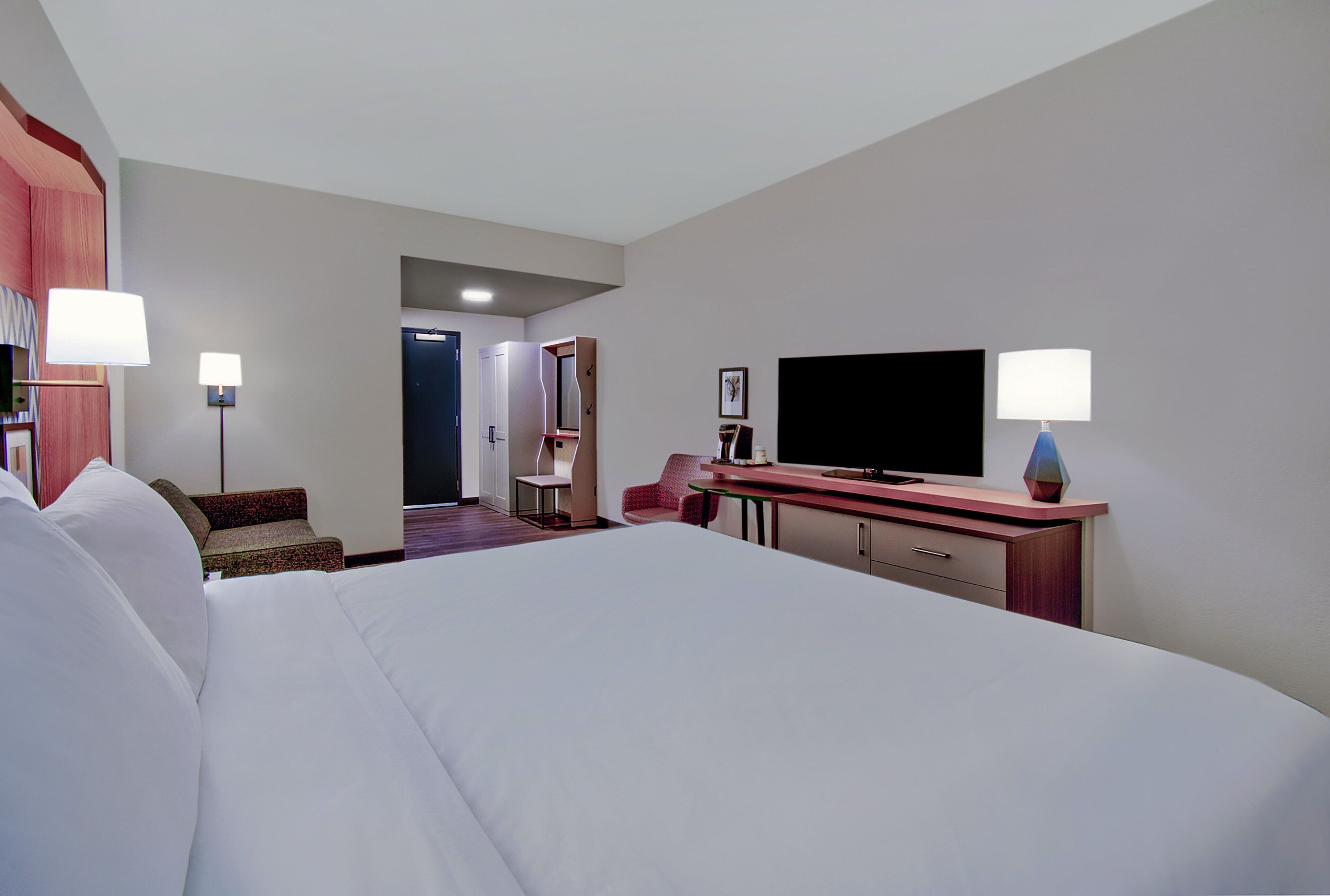 Une chambre d’hôtel avec un grand lit, une télévision, un bureau avec une lampe et une chaise.