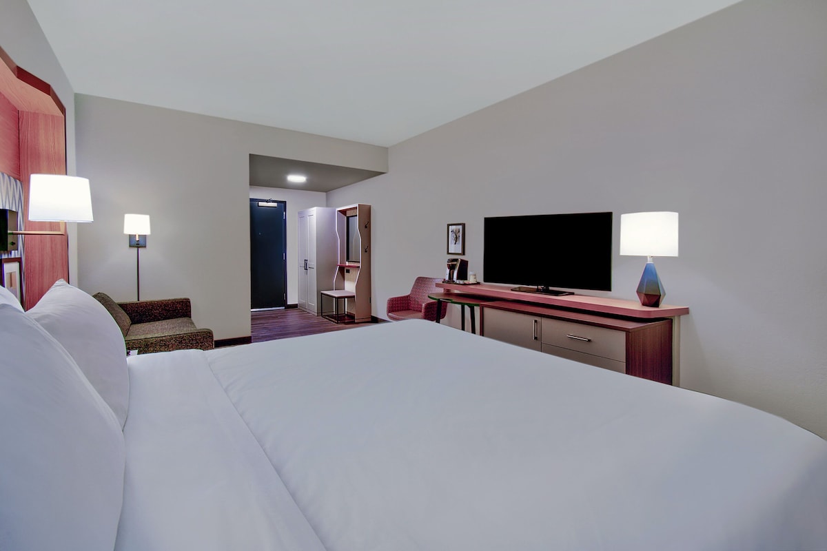 Une chambre d’hôtel avec un grand lit, un téléviseur à écran plat, un bureau avec une lampe et une chaise.