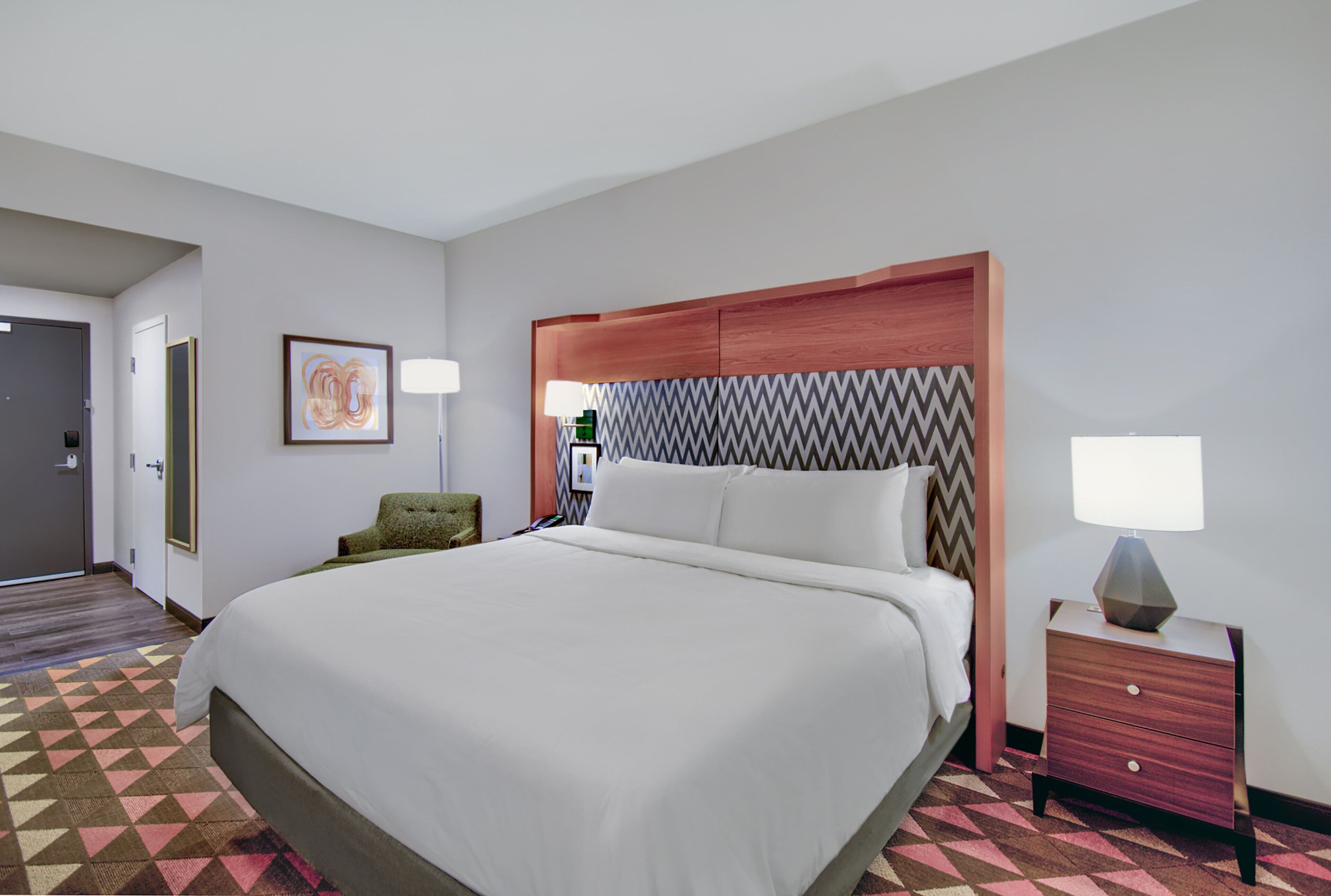 A hotel room with a large bed, a nightstand, a chair, and a door.