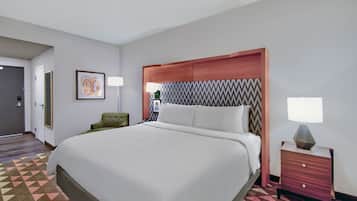 A hotel room with a large bed, a nightstand, a chair, and a door.