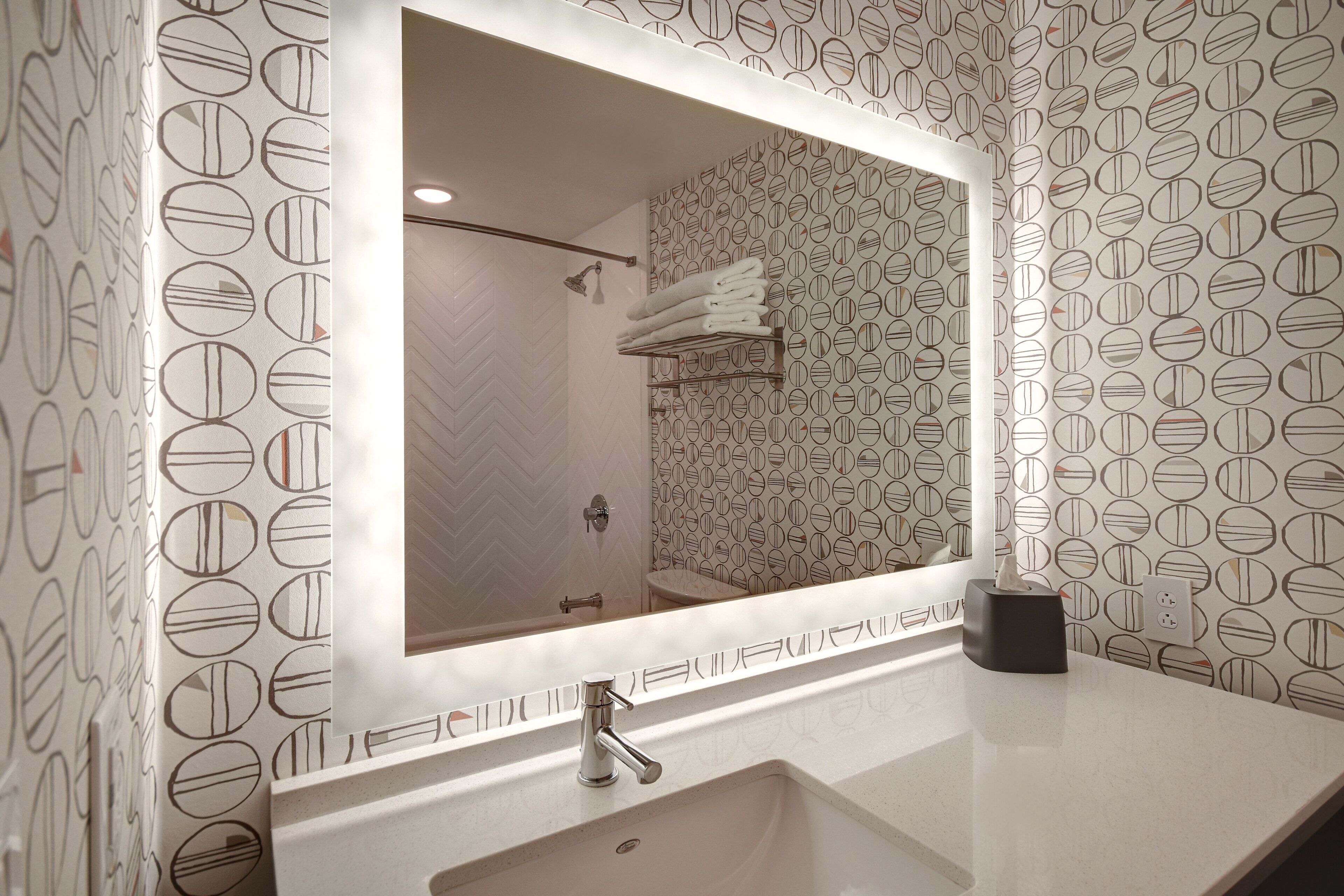A bathroom with a large mirror, a sink, and a shower area.