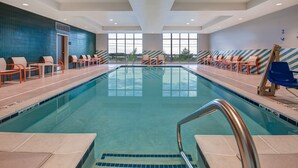 A swimming pool with chairs and a lifeguard stand, large windows, and a view of the outdoors.