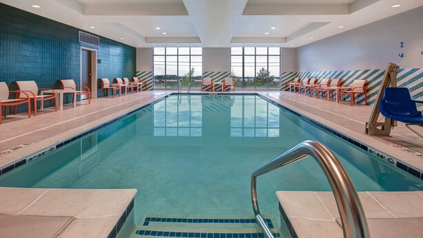 A swimming pool with chairs and a lifeguard stand, large windows, and a view of the outdoors. - Holiday Inn Erie by IHG (Erie)