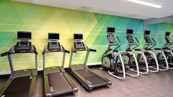 A row of treadmills with digital screens, lined up against a wall with a geometric pattern.