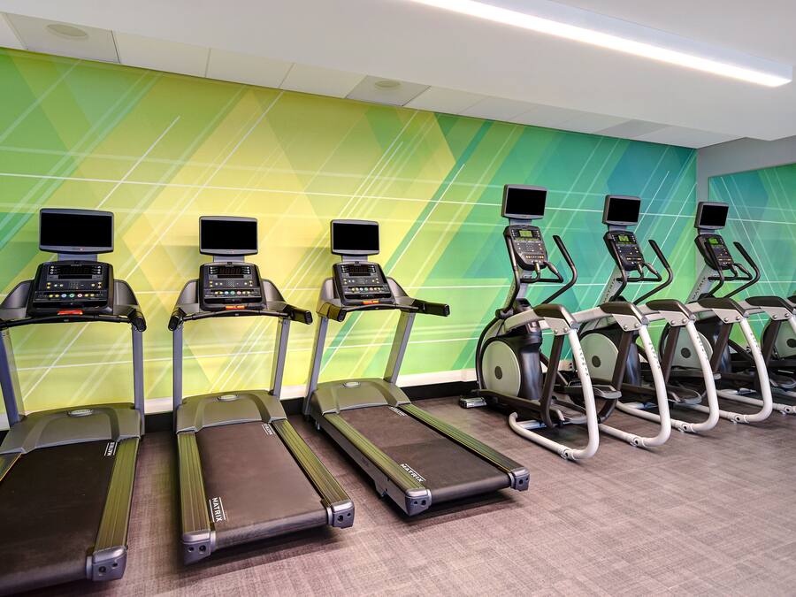 A row of treadmills with digital screens, lined up against a wall with a geometric pattern.