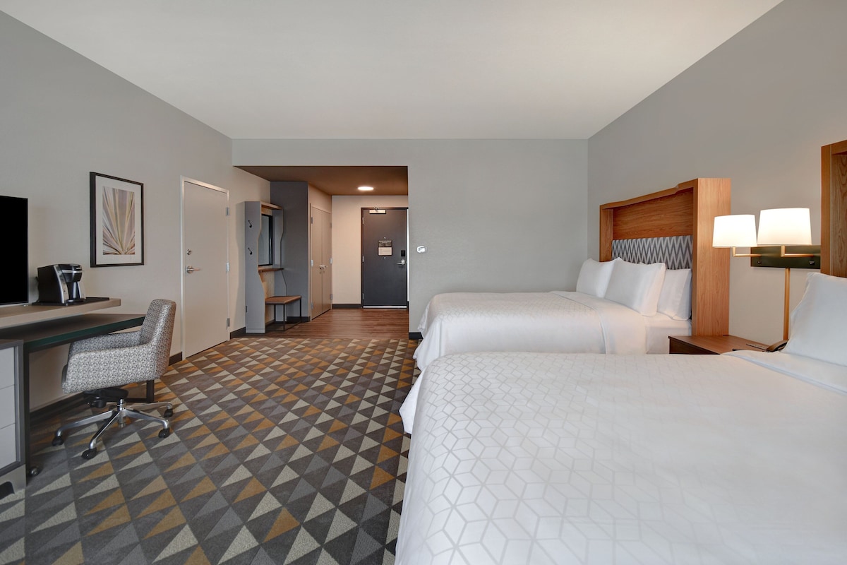 Une chambre d’hôtel avec deux lits, un bureau, une chaise et une moquette à motifs.