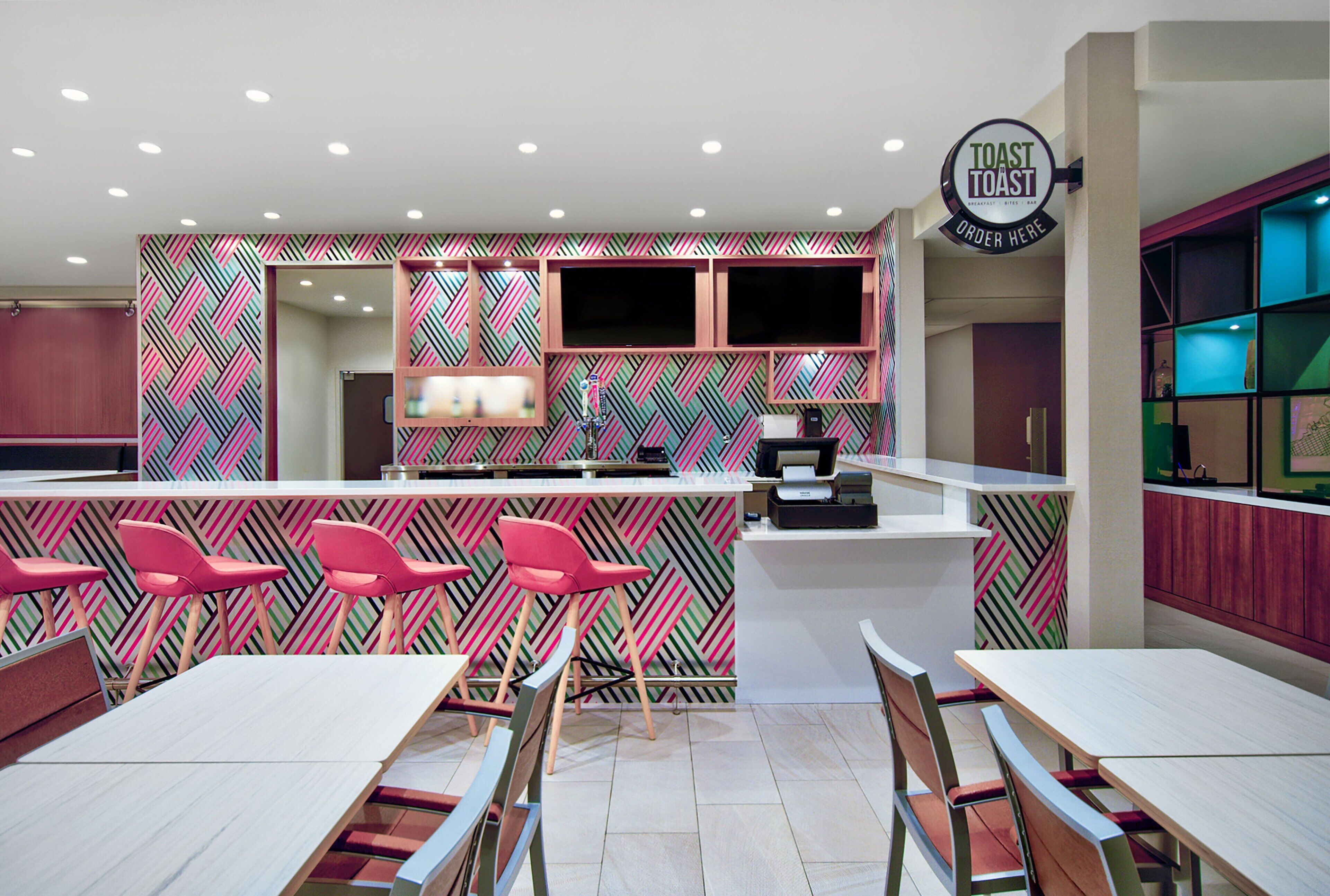 A modern restaurant with a vibrant geometric wall pattern, a central bar area, and multiple seating options including bar stools and tables.