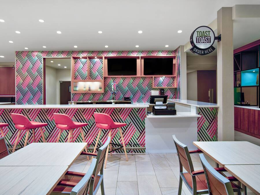 A modern restaurant with a vibrant geometric wall pattern, a central bar area, and multiple seating options including bar stools and tables.