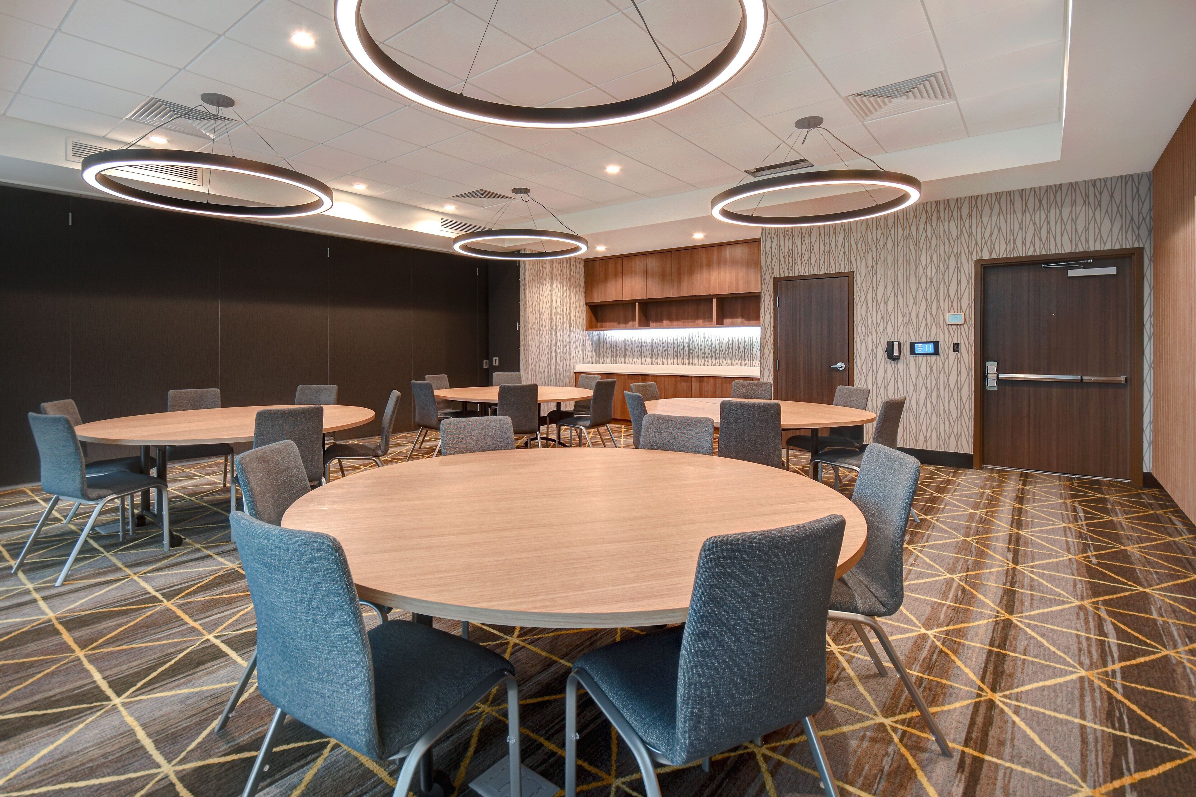 A conference room with round tables and chairs, a patterned carpet, and modern lighting fixtures.