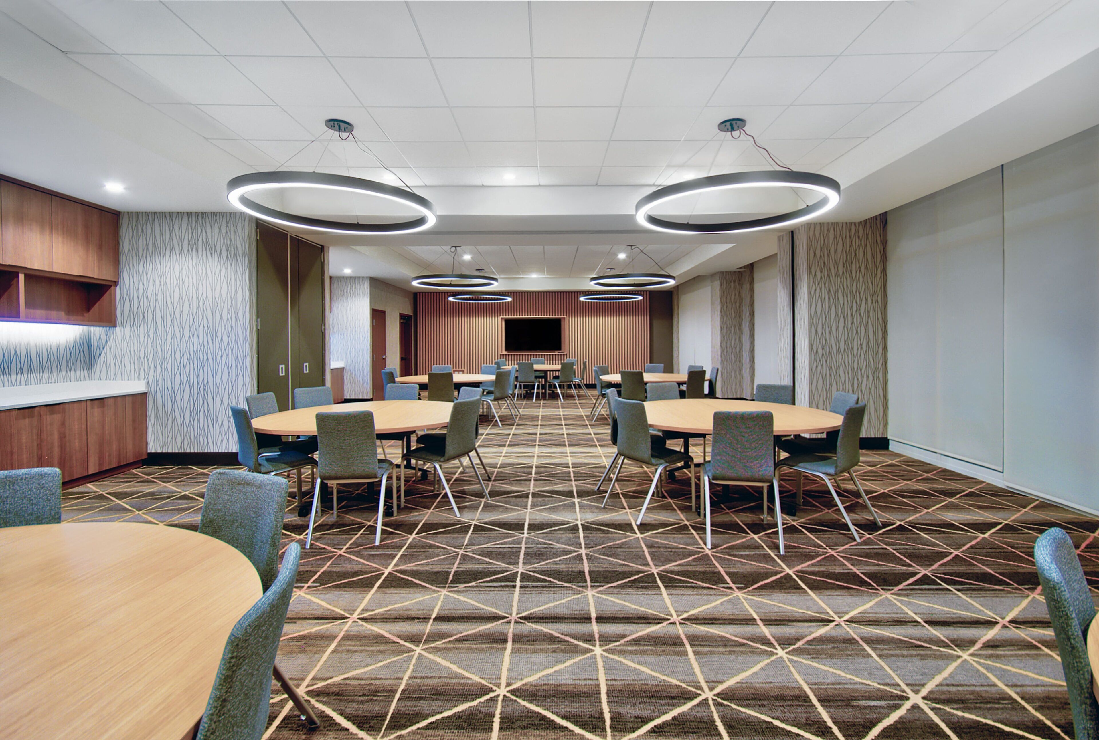 A conference room with multiple tables and chairs, a large screen, and a patterned carpet.