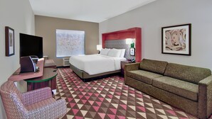 A hotel room with a bed, a sofa, a desk with a computer, a TV, and a large window.