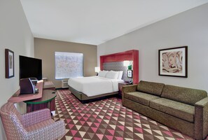 A hotel room with a bed, a sofa, a desk with a computer, a TV, and a large window.