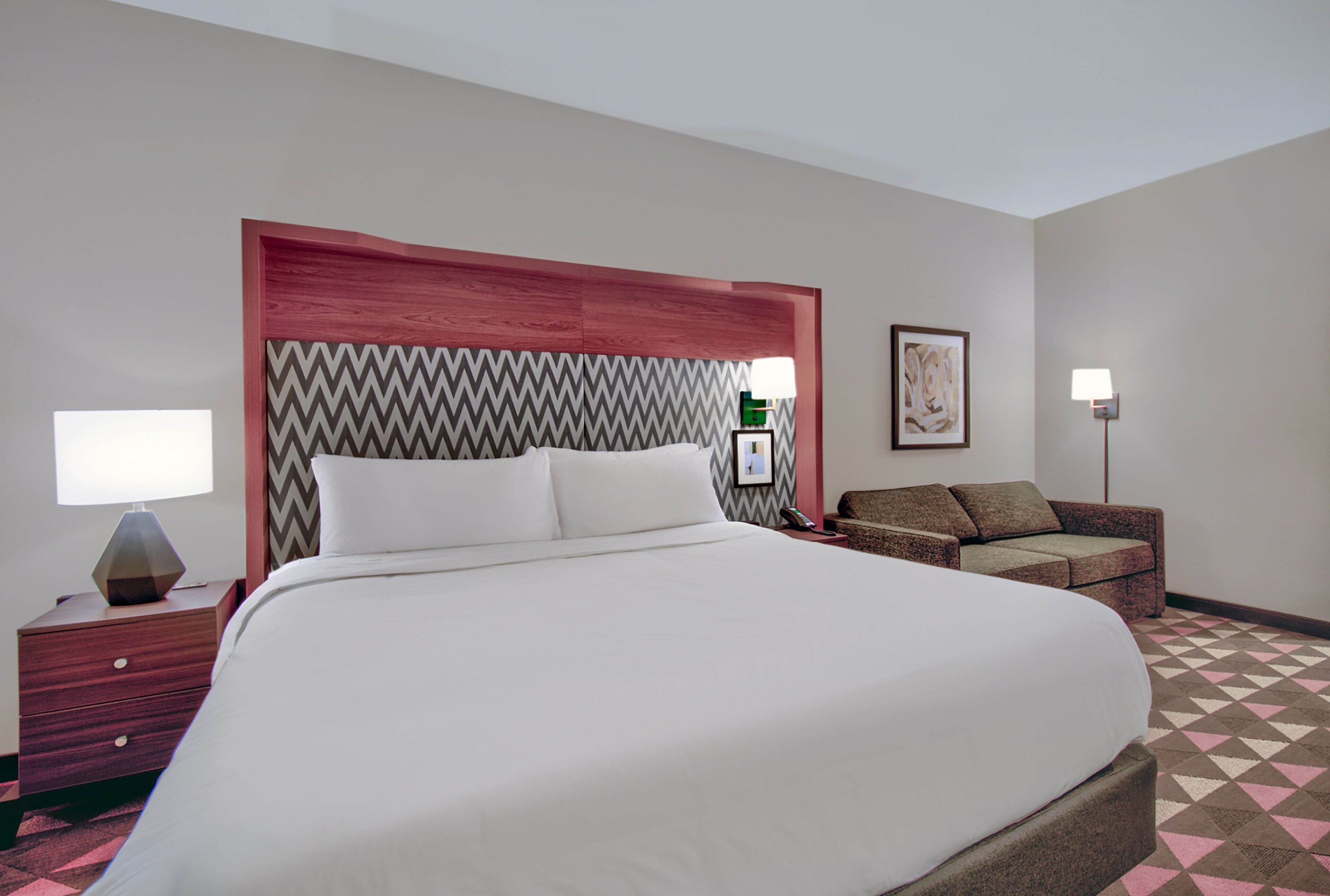 A hotel room with a large bed, bedside tables, a sofa, and a patterned carpet.