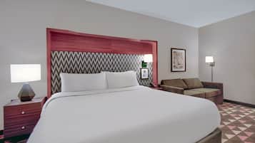 A hotel room with a large bed, bedside tables, a sofa, and a patterned carpet.