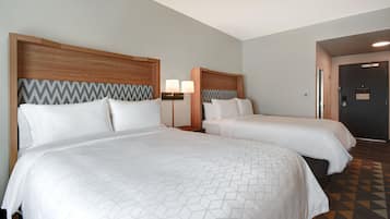 Two beds with wooden headboards and a geometric-patterned bedspread, a nightstand with a lamp, and a patterned carpet.