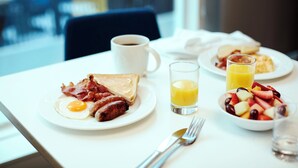 A breakfast table with plates of food, a coffee cup, and a glass of orange juice.
