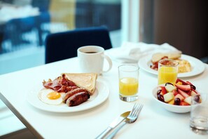 A breakfast table with plates of food, a coffee cup, and a glass of orange juice.