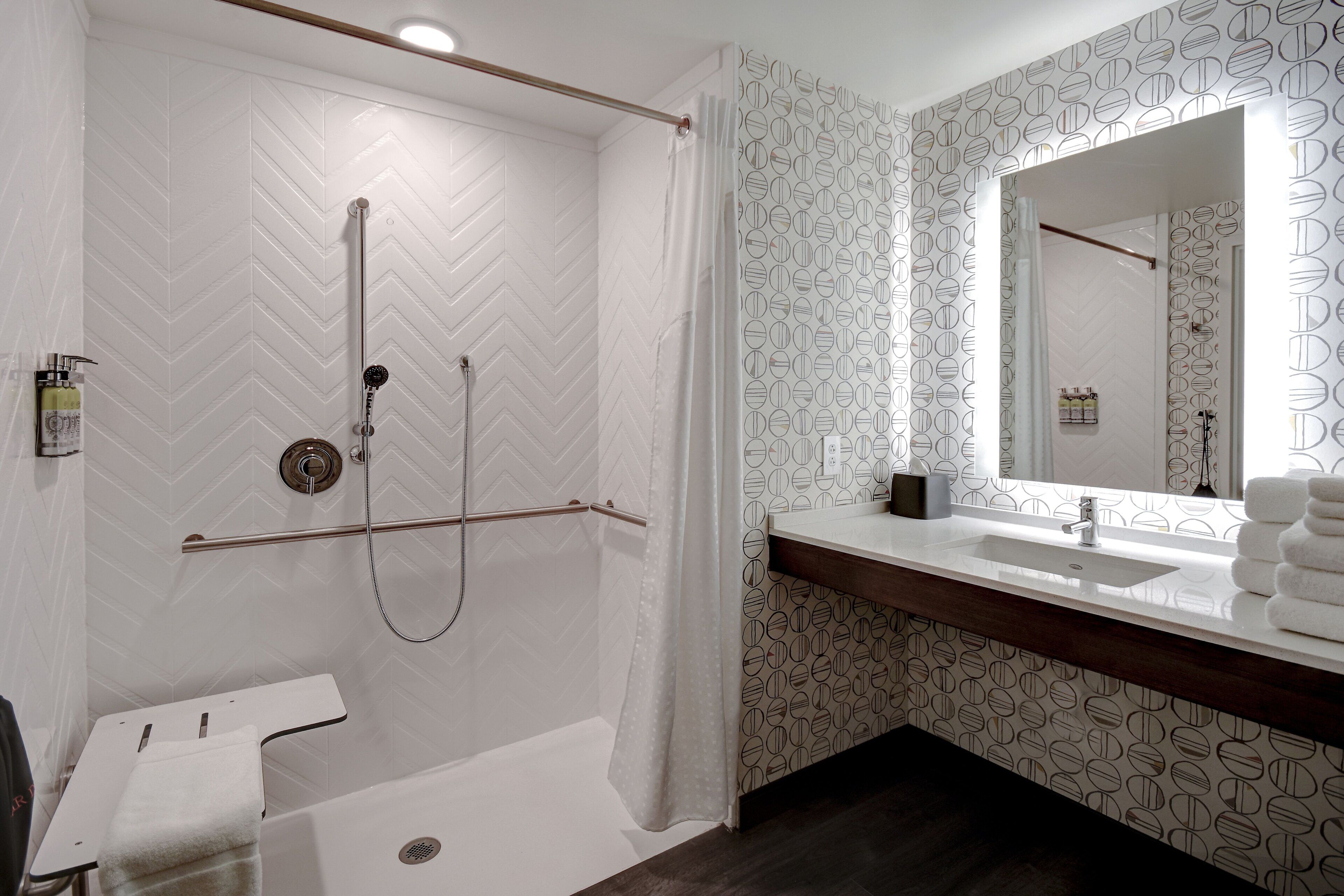 A modern bathroom with a shower, a toilet, a sink, and a mirror.