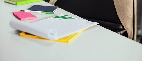 A white table with various items including a green notebook, a pink sticky note, a white paper with green text, and a yellow object.