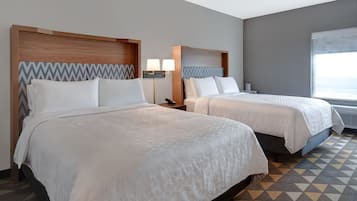 Habitación de hotel con dos camas, cada una con cabecero de madera y un papel tapiz estampado en la pared detrás. Cada cama tiene una mesita de noche con una lámpara y un teléfono.