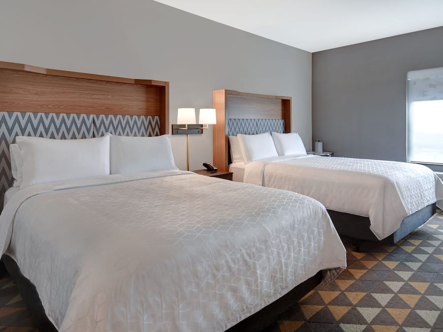 Quarto de hotel com duas camas, cada uma com cabeceira de madeira e parede com padrão decorativo. Em cada cama, um criado-mudo com uma lâmpada e um telefone.