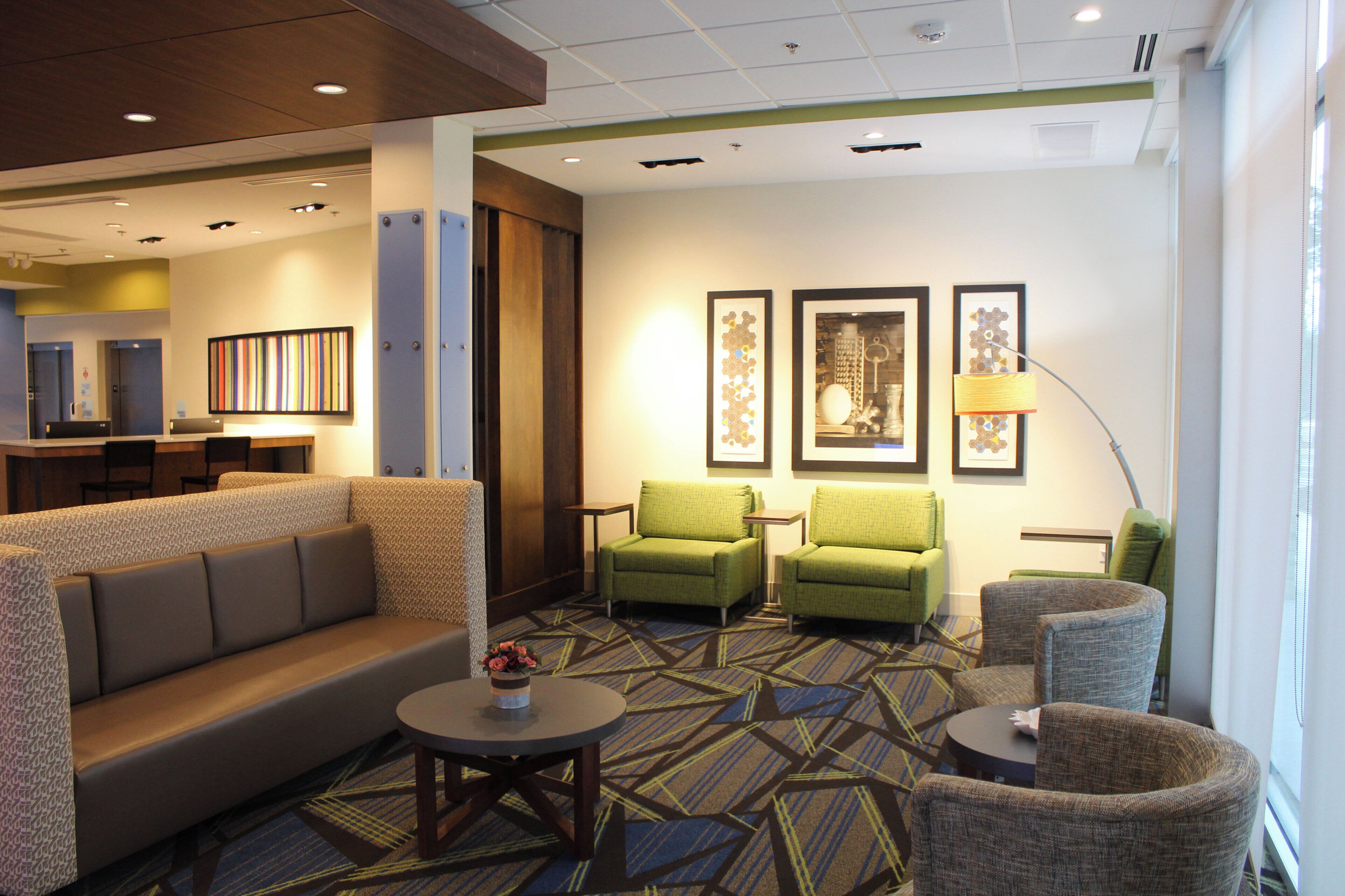 A hotel lobby with a sofa, armchairs, a small table with a vase, and framed artwork on the wall.