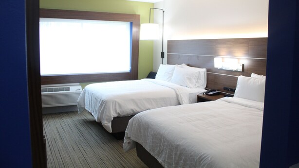 A hotel room with two beds, a window, a wall-mounted lamp, and a bedside table.