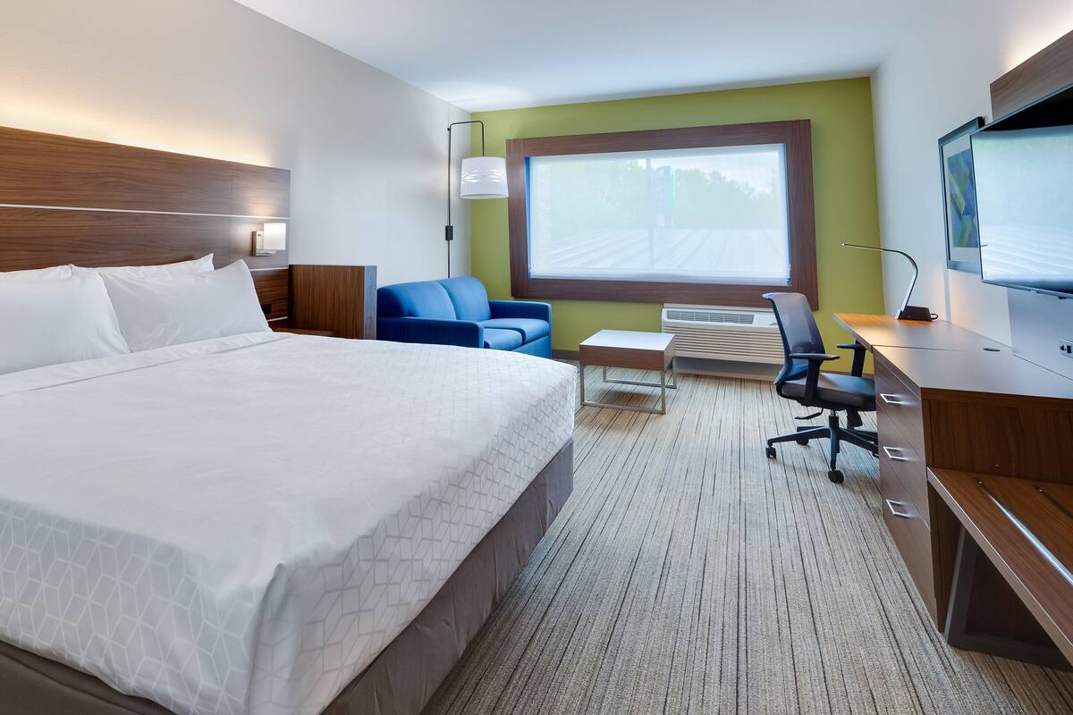 Une chambre d’hôtel avec un grand lit, un bureau avec une chaise, une télévision et une fenêtre donnant sur un beau paysage.