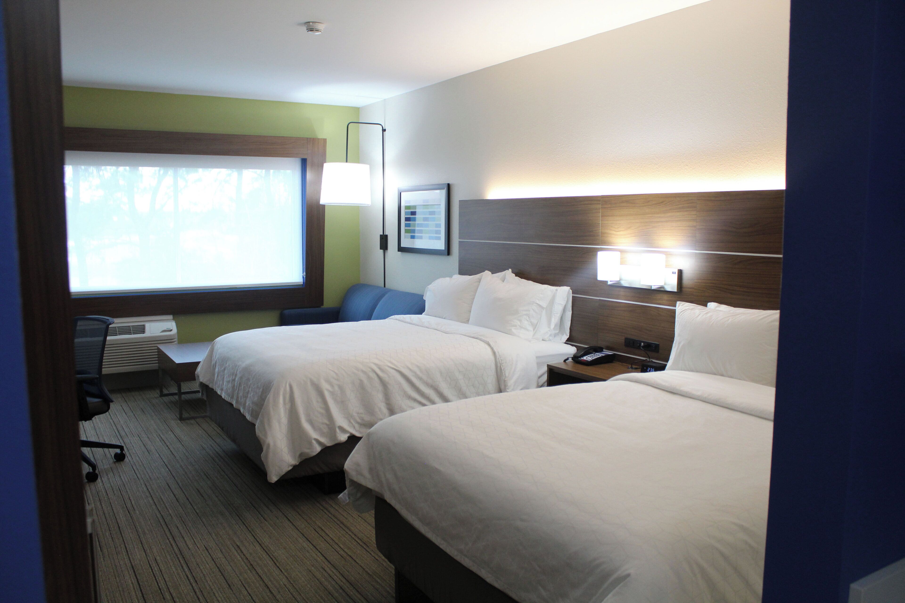 A hotel room with two beds, a desk, a chair, and a window with a view.
