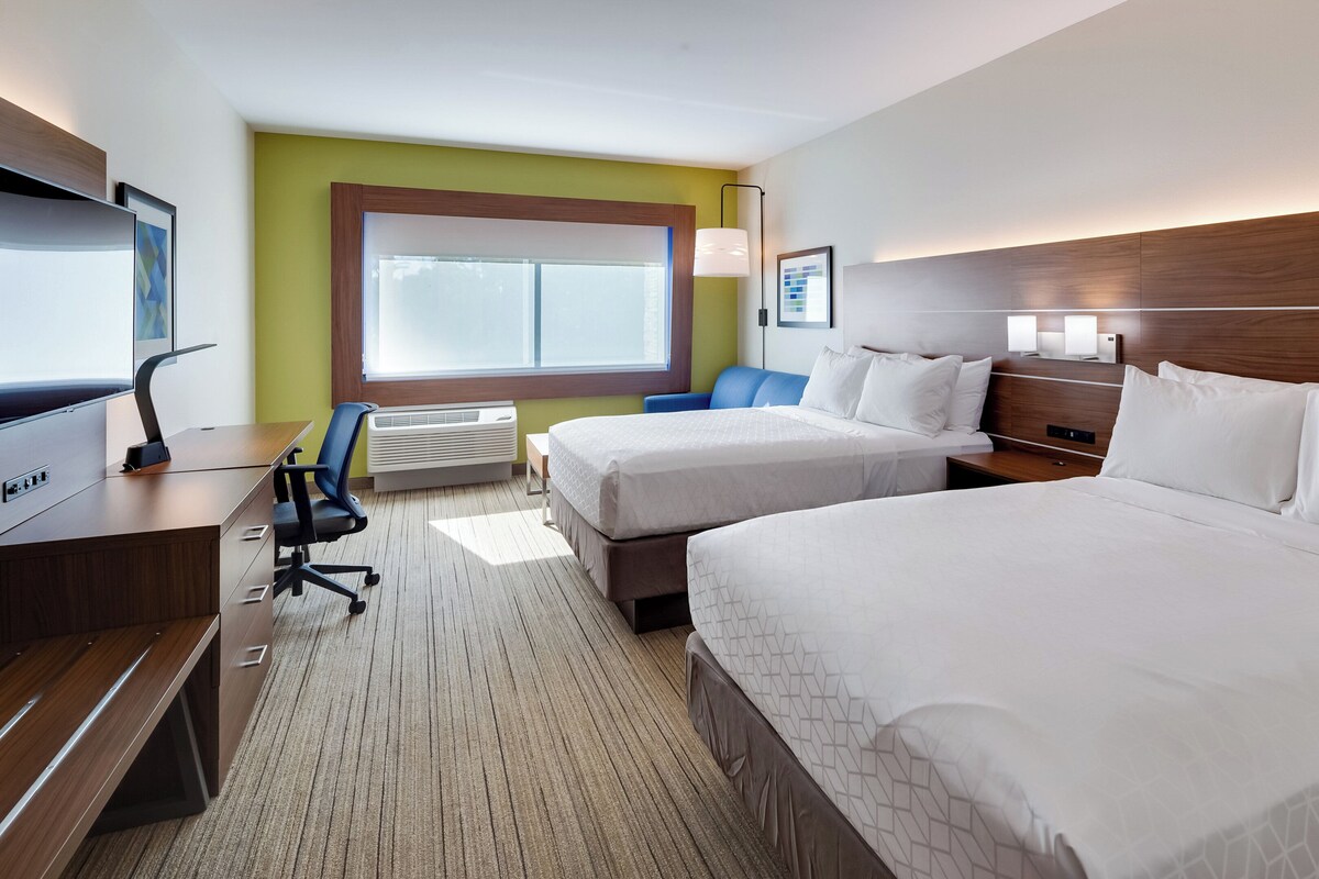 A hotel room with two beds, a desk, a chair, a TV, and a window with blinds.