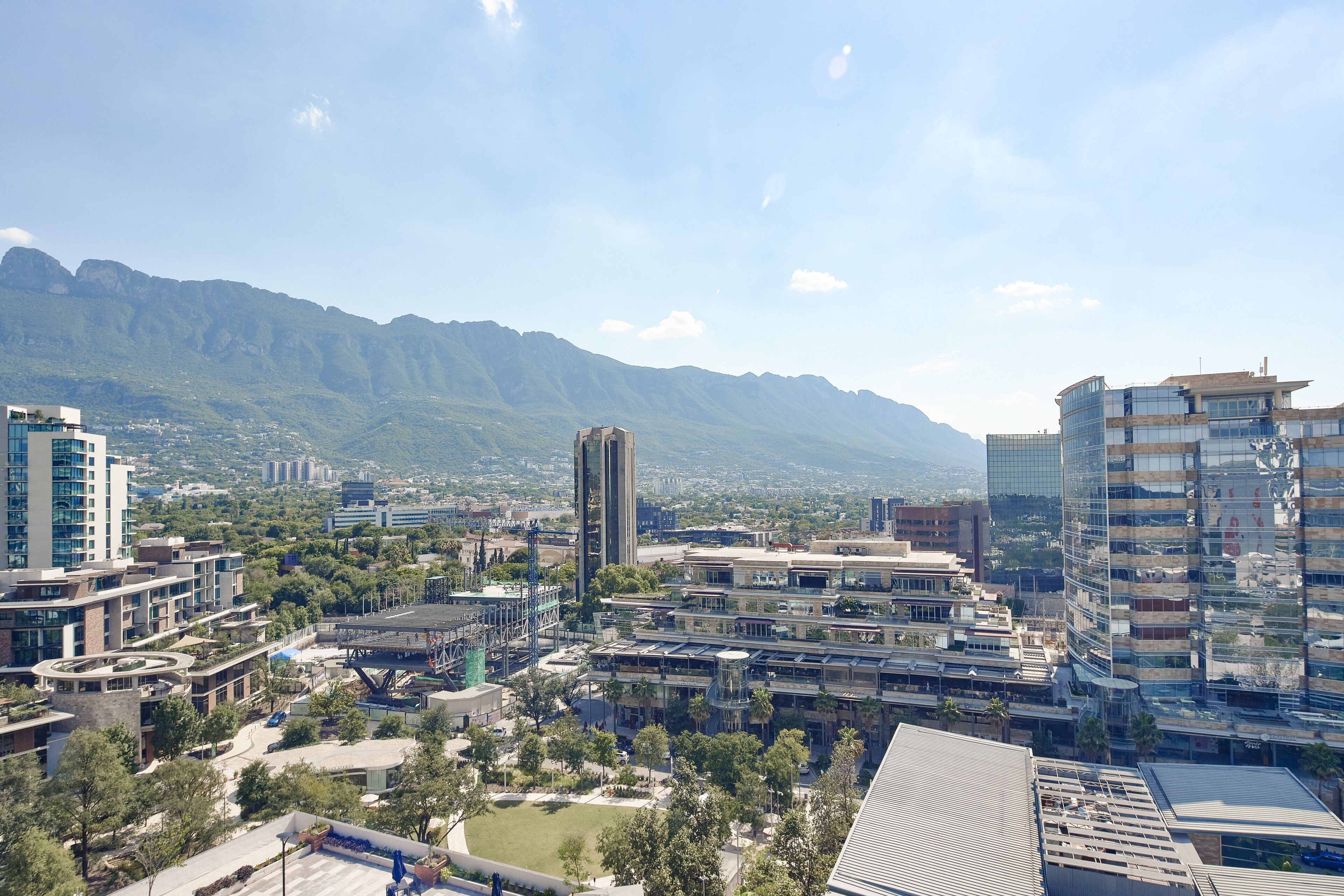 A cityscape with modern buildings, a central plaza, and mountains in the background.