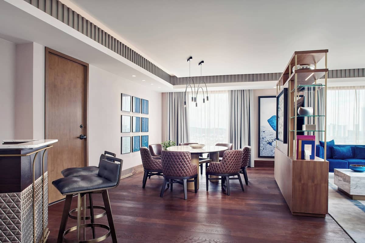 Un salon moderne avec un plancher en bois, un coin repas avec une table ronde et des chaises, un canapé bleu et une bibliothèque.