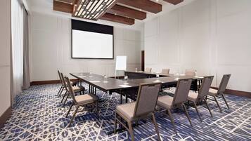 Una sala de conferencias con una gran mesa, sillas y una pantalla para proyector.