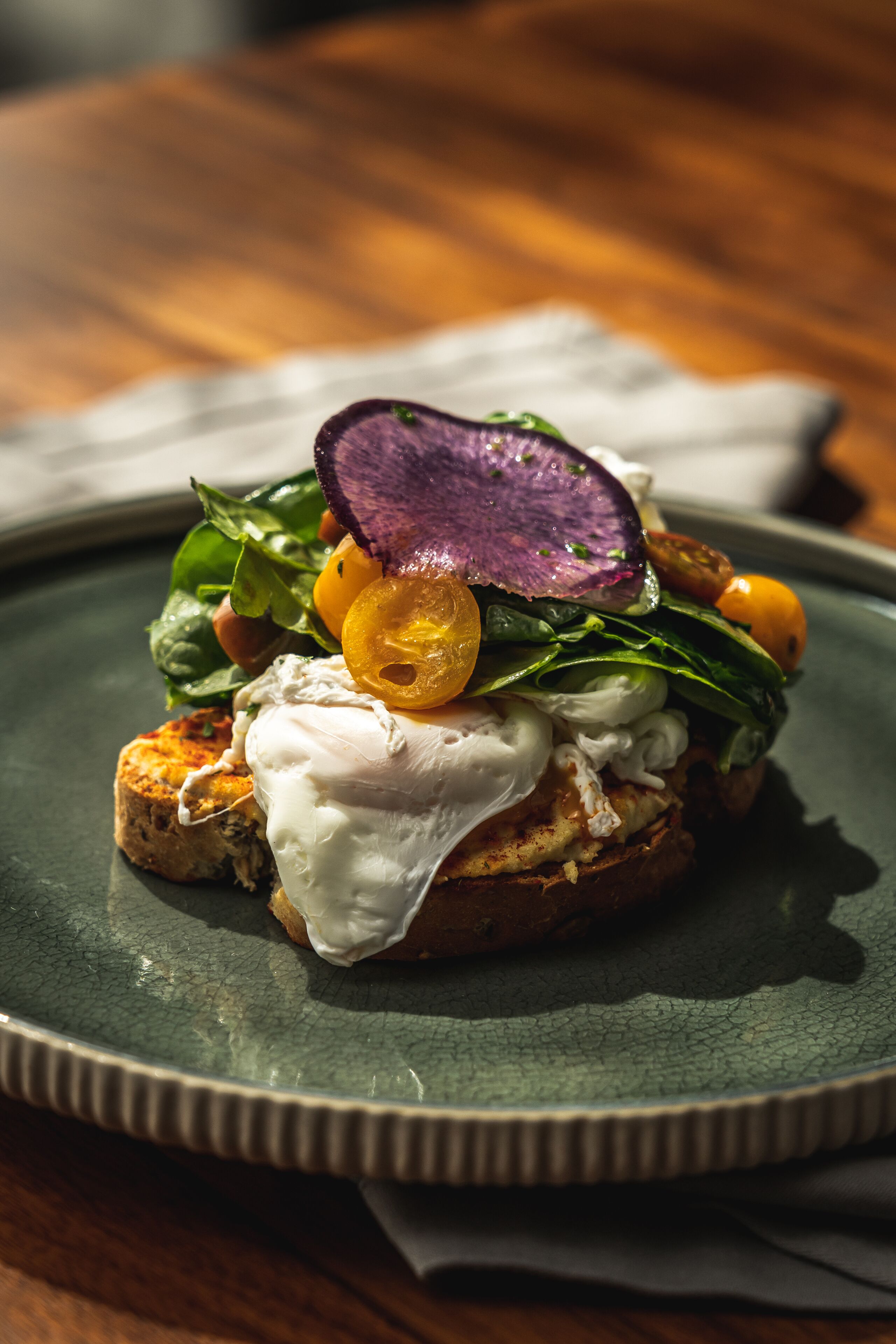 A plate with a sandwich, greens, and a slice of purple vegetable.