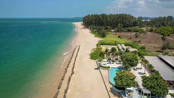 A beach resort with a swimming pool, lounge chairs, and a view of the ocean.