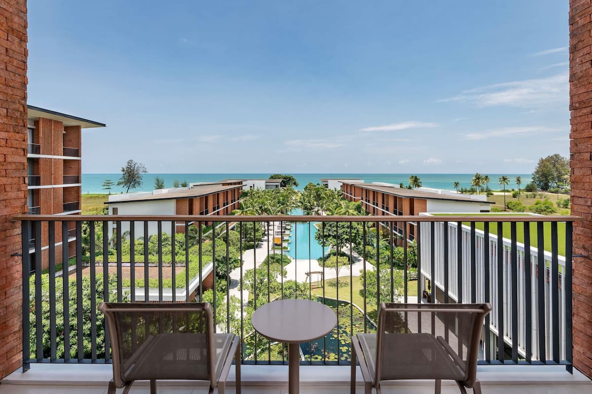 Un balcon avec deux chaises et une table, donnant sur une piscine et une plage.