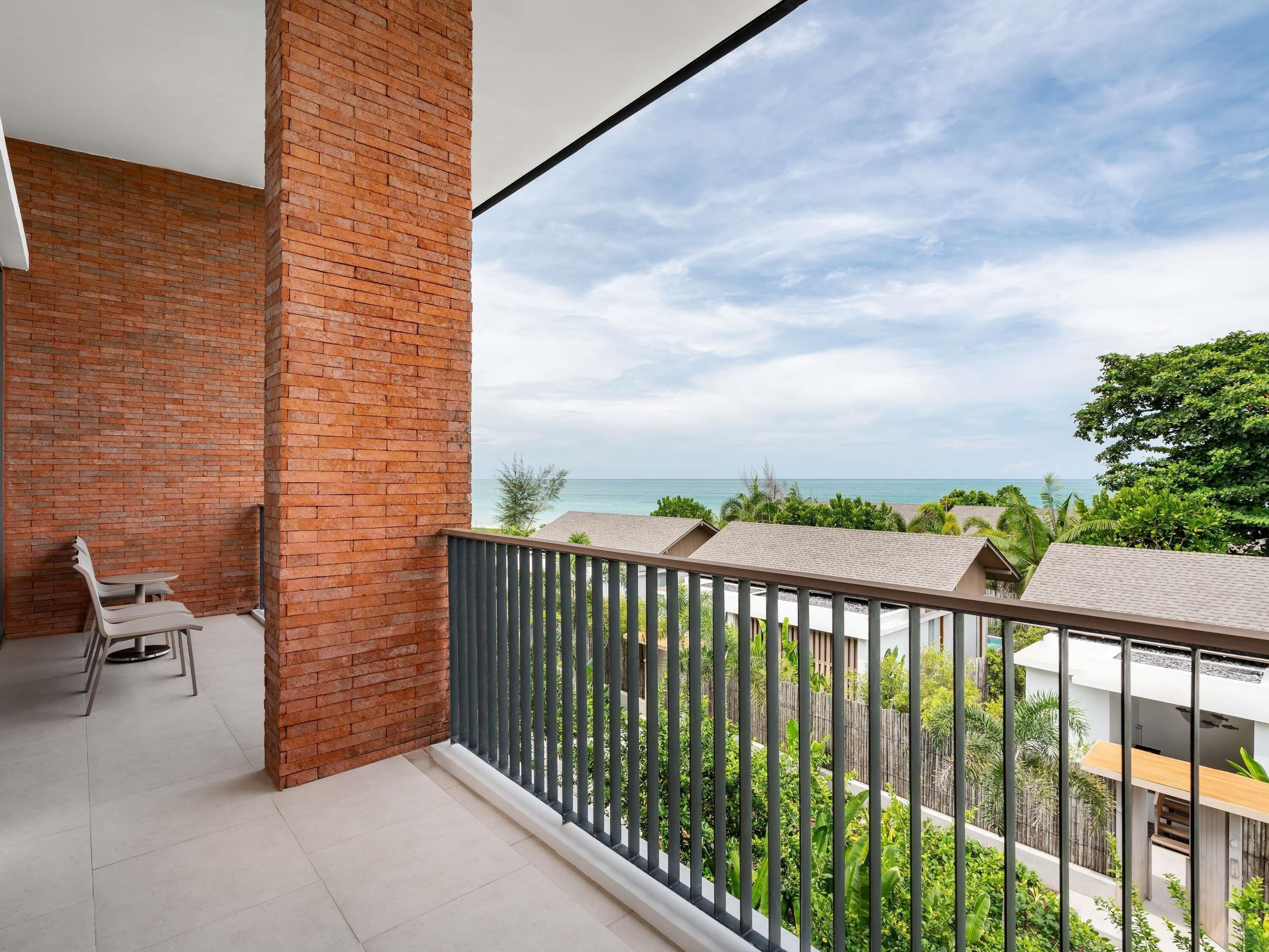 A balcony with a brick wall, a metal railing, and a view of the sea and neighboring buildings.