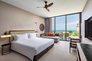 Habitación de hotel con una cama grande, un ventilador de techo, un balcón con vistas al océano y un comedor.