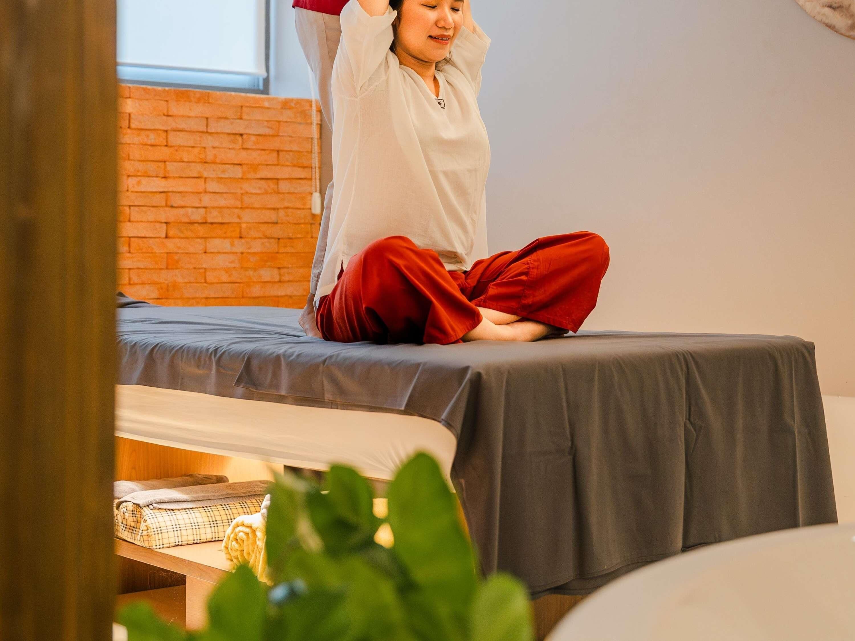 A person sitting on a bed in a room with a brick wall and a window.