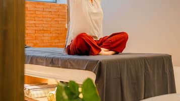 A person sitting on a bed in a room with a brick wall and a window.