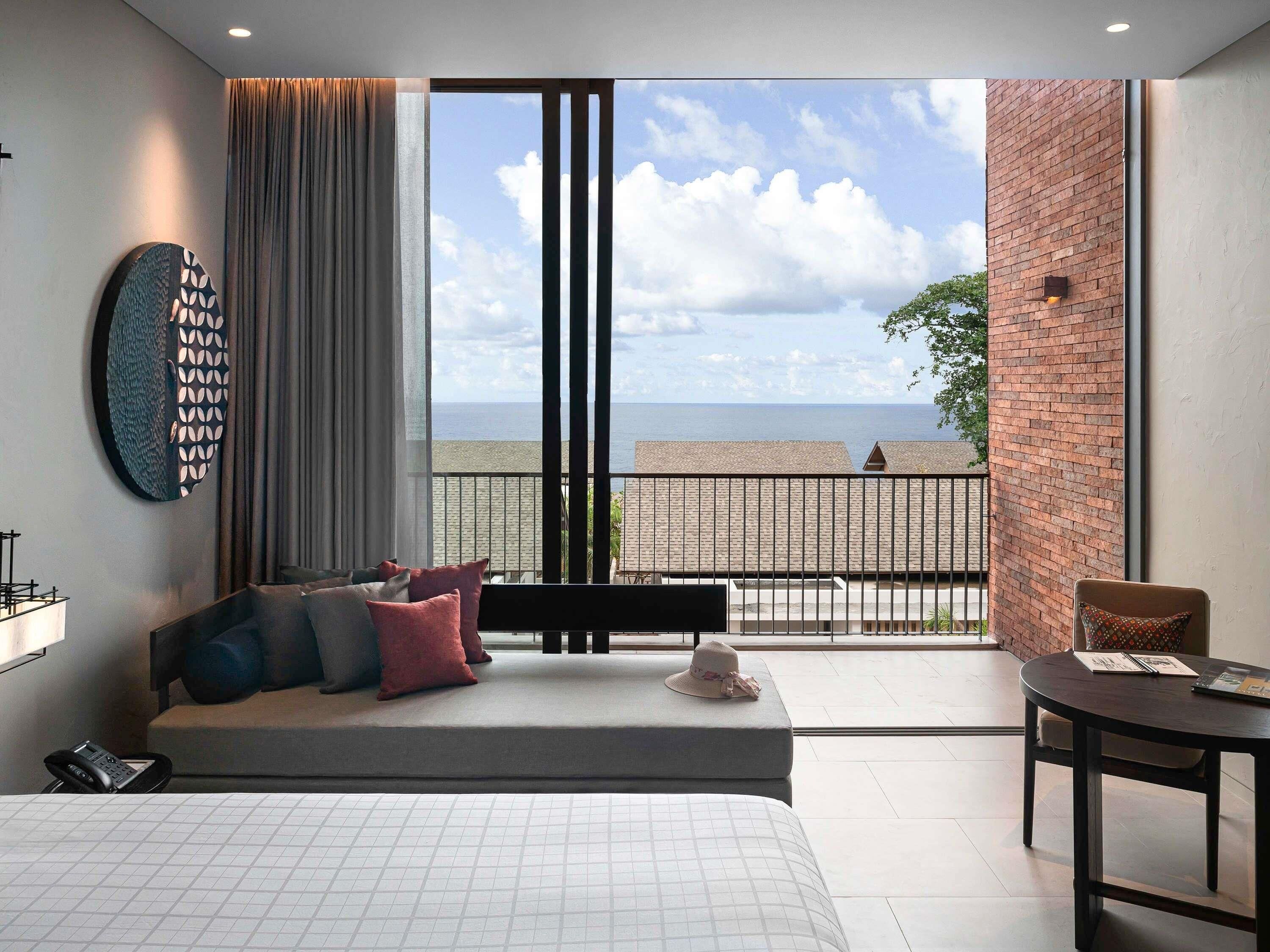 Une chambre d’hôtel moderne dotée d’une grande fenêtre, d’un lit, d’un canapé, d’une petite table et d’un élément décoratif mural.