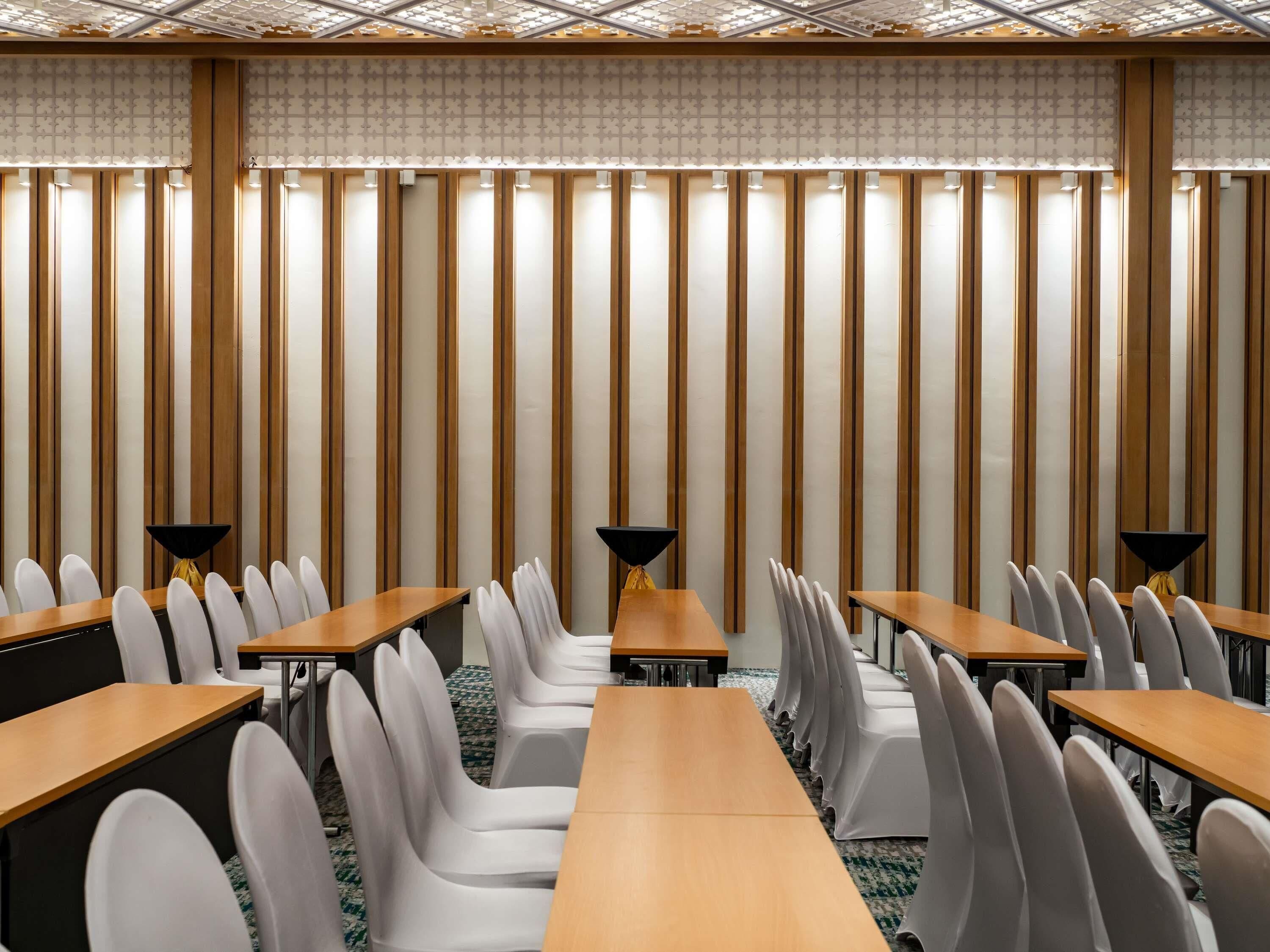 A conference room with long tables and chairs, a patterned wall, and a ceiling with a grid design.