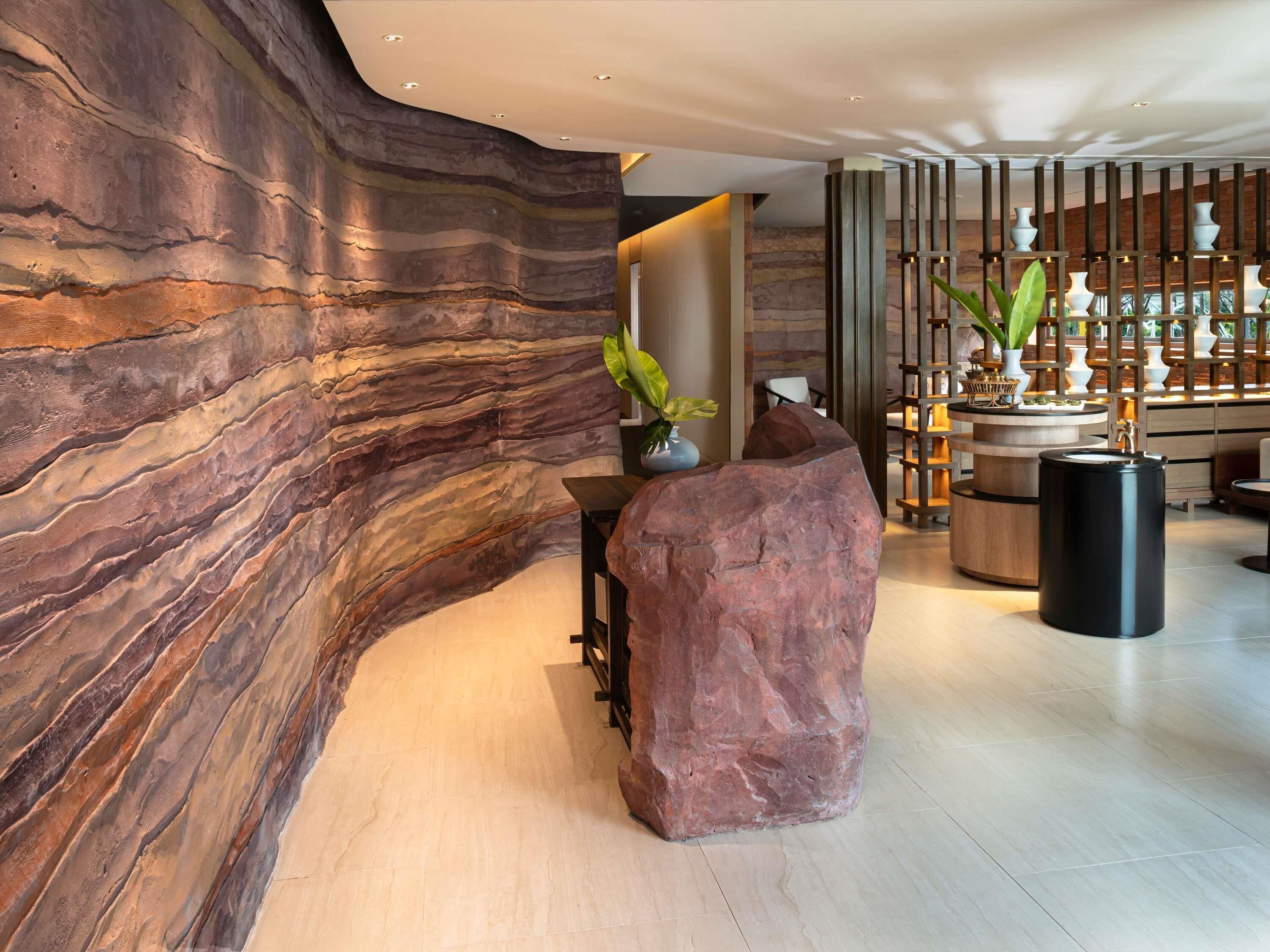 A modern lobby with a large rock feature, a reception desk, and a plant arrangement.