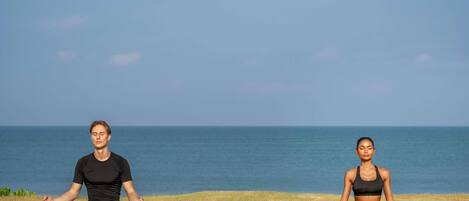 Two individuals meditating on yoga mats by a body of water.